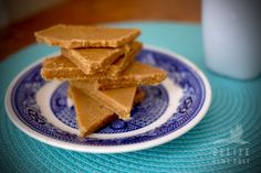 there is a blue and white plate with pieces of peanut butter on it next to a glass of milk