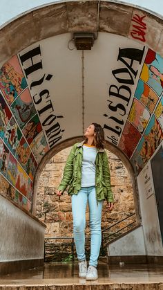 a woman standing in front of an arch with many images on the wall behind her