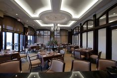 a dining room with tables and chairs, chandelier and windows in the background