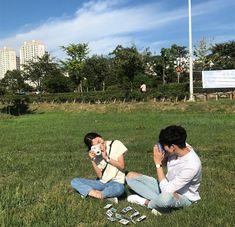 two people sitting on the grass taking pictures