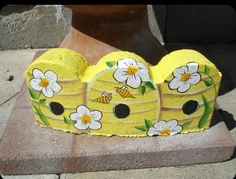 a yellow cake with flowers and bees on it sitting on a stone slab next to a potted planter