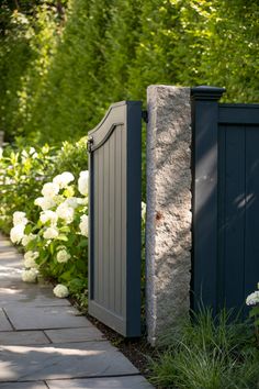 a stone wall and gate in front of white flowers on the side of a path