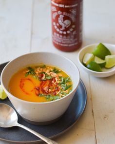 a bowl of soup on a plate next to a jar of ketchup and limes