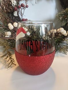 a red wine glass sitting on top of a table next to a christmas wreath and pine branches