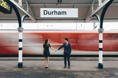 a man and woman holding hands in front of a train