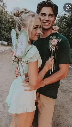 a man standing next to a woman with a fairy wings on her shoulder and holding a flower