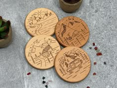 four wooden coasters with drawings on them sitting next to some succulent plants