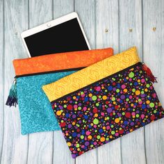 three different colored clutches sitting next to each other on top of a wooden table with an electronic device in it