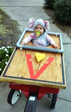 a baby is sitting in a wagon with cheese on the side and an elephant hat