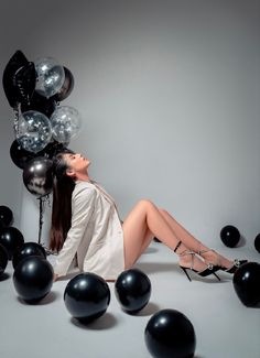 a woman laying on the ground surrounded by black and silver balloons with her legs crossed