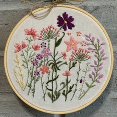 the embroidery is hanging on the wall and there are flowers in it, all different colors