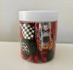 a jar filled with assorted race cars on top of a white table next to a wall