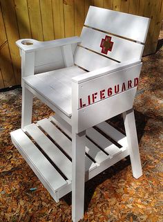 a white lifeguard chair sitting on top of leafy ground next to a wooden fence