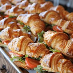 many croissants with tomatoes and lettuce are lined up on a tray