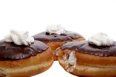 three doughnuts with chocolate icing and whipped cream on top, sitting side by side