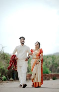 a man and woman are walking down the street holding red flowers in their hands while dressed in white