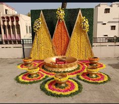 an elaborate flower arrangement in front of a building with candles and flowers on the ground