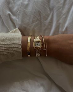 a person wearing three different bracelets and a watch on their arm with white sheets in the background