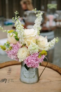 a bouquet of white and pink flowers sitting in a metal vase on top of a wooden barrel