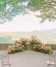 two chairs sitting on top of a gravel covered field next to a lush green hillside