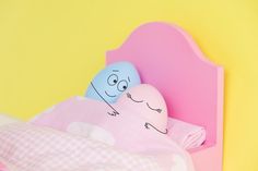 two pillows sitting on top of a pink and blue headboard next to a yellow wall