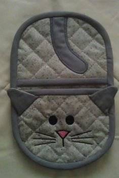 an oven mitt with a cat design on it's face and eyes, sitting on a bed