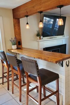 a bar with four stools and a television mounted on the wall above it in a living room