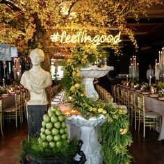 there is a table set up with fruit and greenery in front of a statue