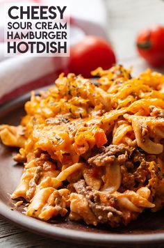 a plate full of cheesy hamburger hotdish with tomatoes in the background