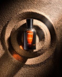 an orange bottle sitting in the middle of a spiral design on sand with sunlight coming through it