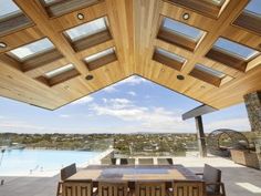 an outdoor dining table and chairs under a wooden roof over looking a large swimming pool