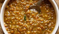 a white bowl filled with beans on top of a wooden table next to a spoon