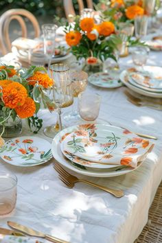 the table is set with orange flowers and plates