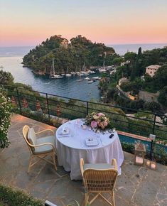 an outdoor dining table with two chairs and a view of the water at sunset or dawn