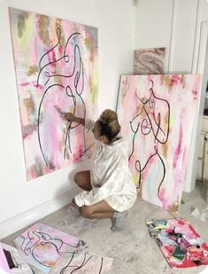 a woman kneeling down in front of two large paintings on the wall and painting them