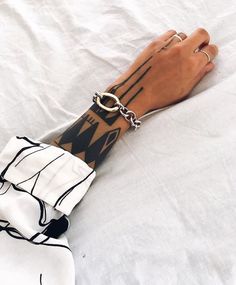 a person's arm with tattoos on it laying on a white sheet covered bed