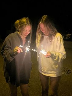 two girls standing next to each other holding sparklers