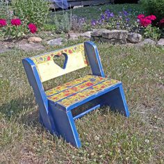 a blue and yellow wooden chair sitting on top of a grass covered field next to flowers