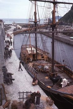 an old pirate ship is docked at the dock while people are walking around it and onlookers watch