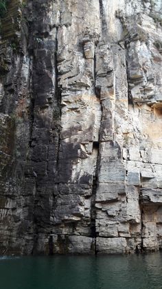 a large rock face next to a body of water