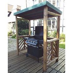 an outdoor grill on a deck with a gazebo in the back ground and grass behind it