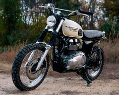 a motorcycle is parked on the dirt near some bushes and trees in the background,