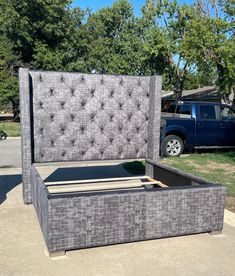 an upholstered bed frame in the middle of a driveway with a truck parked behind it