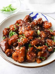 a white plate topped with chicken covered in sesame seeds and garnished with green onions