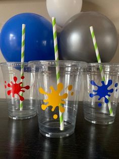 four cups with colorful straws and balloons in the background