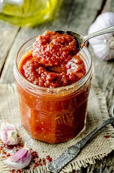 a spoon full of sauce sitting on top of a table next to garlic and pepper