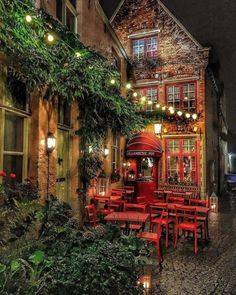 an outdoor restaurant with red chairs and tables in front of the building at night time