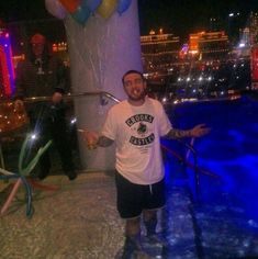 a man standing in front of a pool at night with balloons and streamers around him