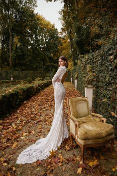 a woman in a white wedding dress standing next to a chair and ivy covered wall