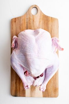 a raw chicken sitting on top of a wooden cutting board next to a white wall